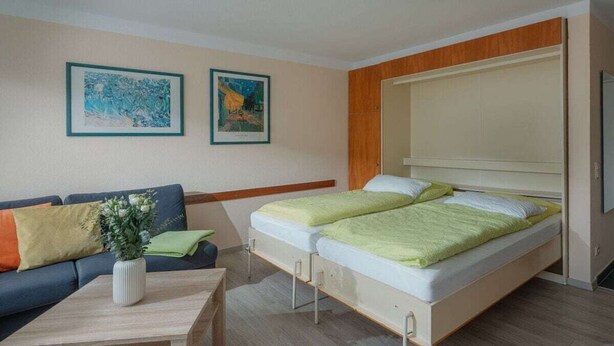 Ett modernt sovrum med en säng, en soffa, ett soffbord och två inramade konstverk på väggen.