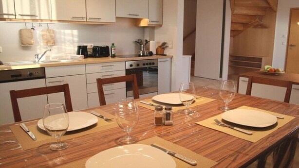 Una cucina moderna con mobili bianchi, un piano di lavoro in legno e un tavolo da pranzo per quattro persone, apparecchiato con calici e piatti.