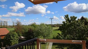 Vista da un balcone con ringhiera in legno, su un paesaggio verde con alberi e cielo sereno.