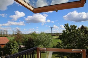 Blick von einem Balkon mit Holzwertung auf eine grüne Landschaft mit Bäumen und blauem Himmel.