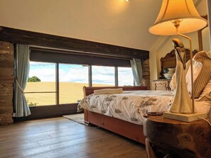 A bedroom with a large window, wooden flooring, a bed with a floral bedspread, and a bedside lamp. - The Warm Hearth: 15 Acre Countryside Estate (Hereford)