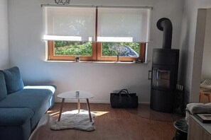 A cozy room with a sofa, a small round table, a window with blinds, and a wood-burning stove. - Oasis in the Rehgebirge mountains (Donzdorf)