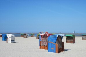 A beach with rows of beach huts, some with numbers on them, and a clear blue sky. - Holiday home with 2 bedrooms (Nessmersiel)