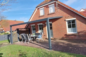 Une maison en briques avec un patio couvert, une table et des chaises, et un petit jardin.