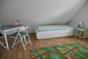 Une chambre d’enfant avec un lit, un bureau, une chaise et un tapis de jeu coloré.