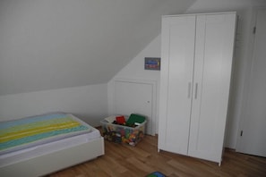 A bedroom with a bed, a wardrobe, and a storage box with toys. - Holiday home with 2 bedrooms (Nessmersiel)
