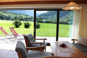 A room with a view of a green field and mountains, a table with a placemat, and two red lounge chairs. - Holiday apartment with 2 bedrooms (Schönau am Königssee)