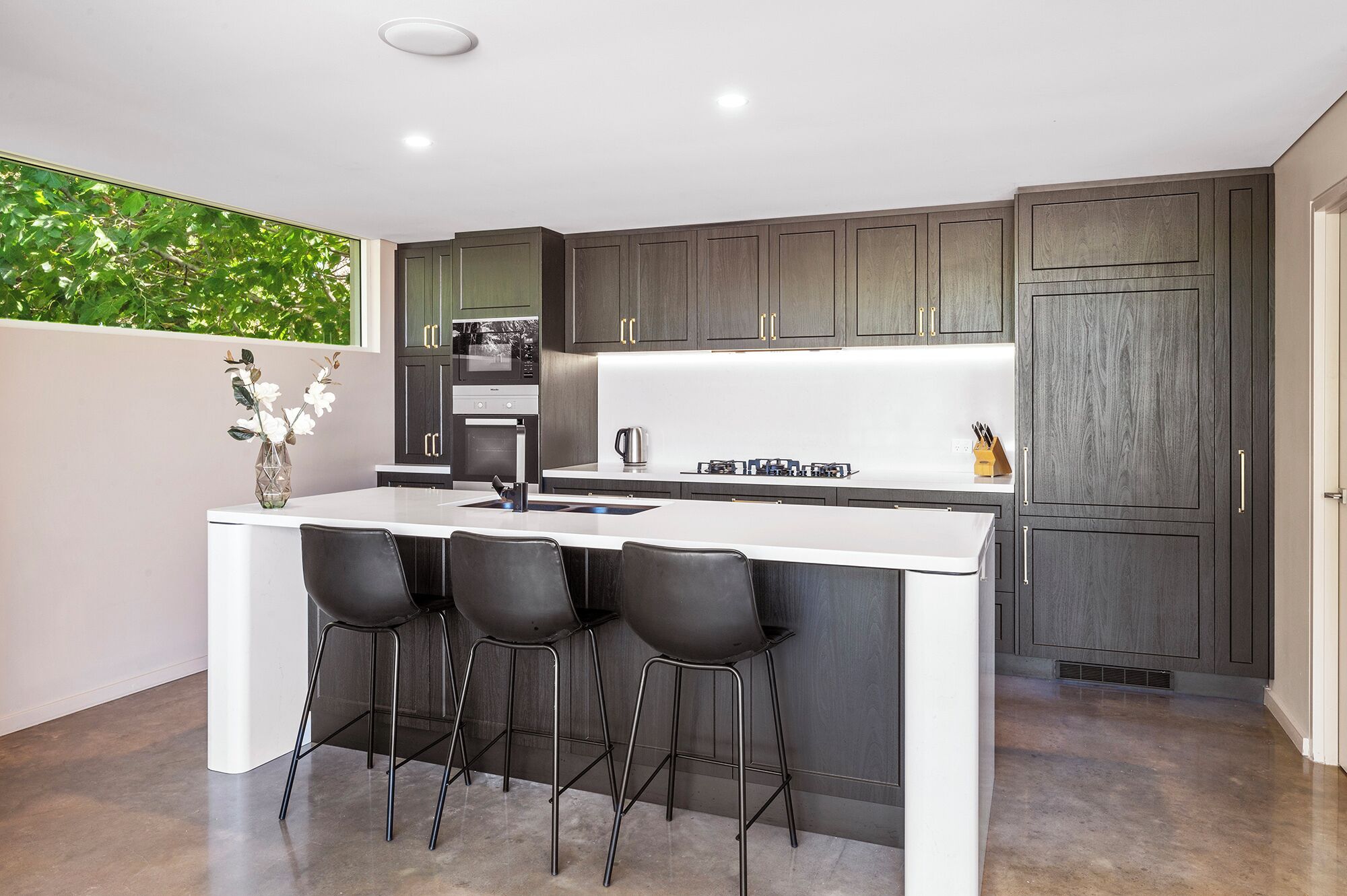 A modern kitchen with a central island, bar stools, and dark wood cabinetry.