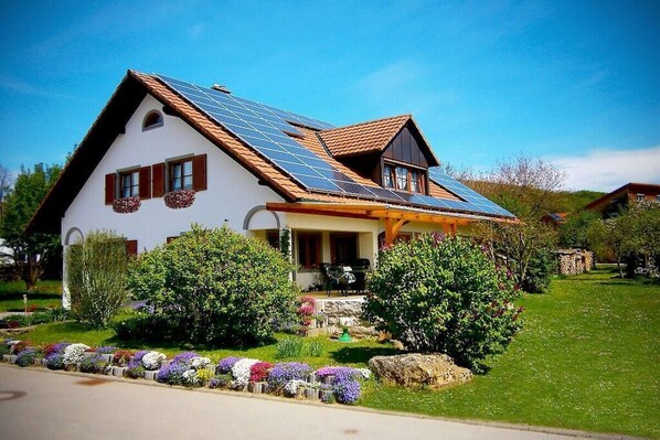 Een huis met een schuin dak, zonnepanelen en een verzorgde tuin met diverse planten en bloemen.