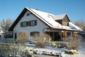Een herenhuis met twee verdiepingen, een schuine kap, houten luiken en een overdekte veranda.