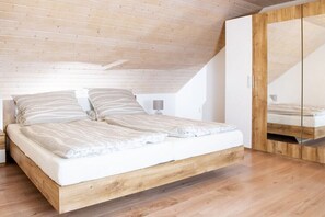 Een slaapkamer met een houten bedframe, een witte matras en een houten garderobe.