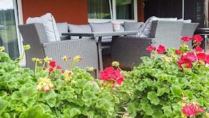 An outdoor seating area with wicker furniture and a table, surrounded by green foliage and red flowers. - Apartment in Forstau with sauna and balcony (Forstau)