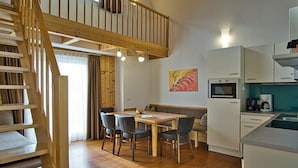 A modern kitchen with a dining area, wooden staircase, and a painting on the wall. - Apartment in Forstau with sauna and balcony (Forstau)