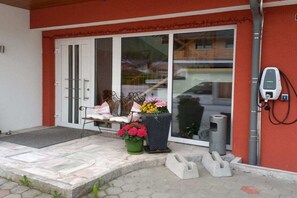 Ein Gebäudeeingang mit roter Wand, weißer Tür und einer Bank mit Blumentöpfen.