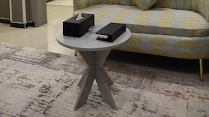 Een kamer met een bank, een klein rond tafeltje met zakdoos en afstandsbediening, en een kamerkleed met een patroon.