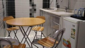 Een kleine keuken met een ronde tafel en vier stoelen, een koelkast en een spoelbak.