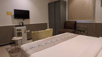 A hotel room with a bed, a television, a wardrobe, a chair, and a small table.