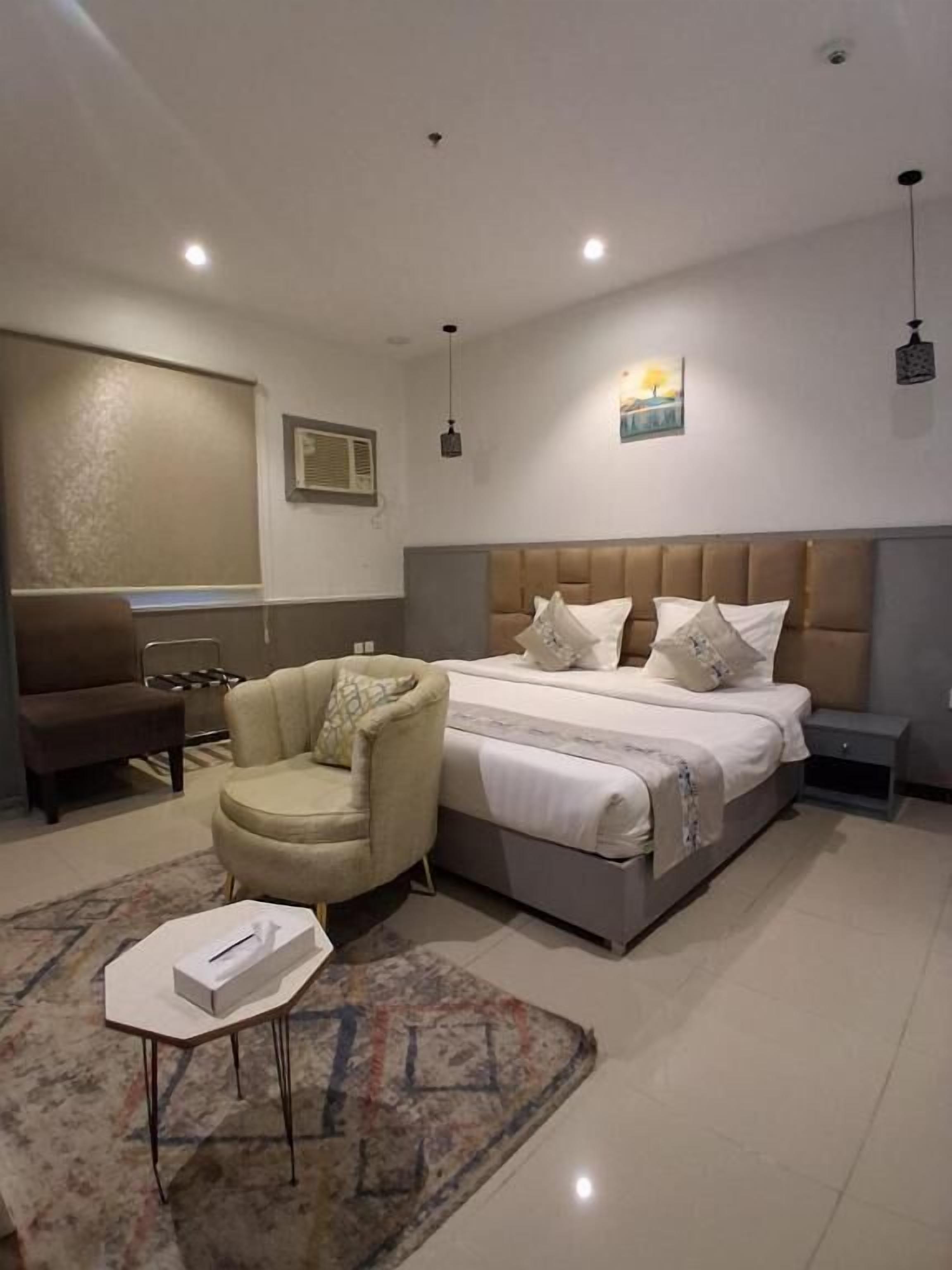 Quarto moderno com cama grande, uma cadeira, mesa de cabeceira e criado-mudo.
