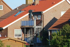 A residential building with a red-tiled roof, a visible staircase leading to a balcony, and a window with a white frame.