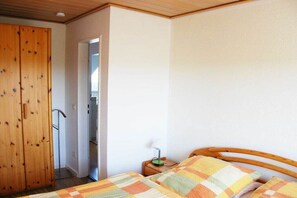 A bedroom with a wooden wardrobe, a bed with a checkered blanket, and a nightstand with a lamp. - Holiday apartment in Juist with swimming pool (Juist)