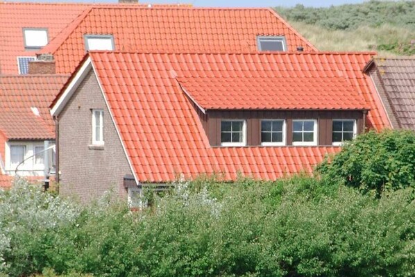 A residential building with a red-tiled roof, multiple windows, and a visible chimney.