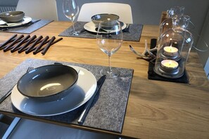 Ein Esstisch gedeckt mit Tellern, Besteck und Gläsern, mit Kerzen und einem Glasbehälter daneben.