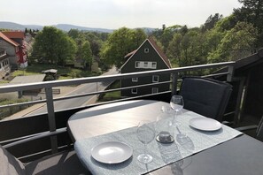 A balcony with a table set for two, overlooking a residential area with houses and trees. - Holiday apartment with 2 bedrooms (Sankt Andreasberg)