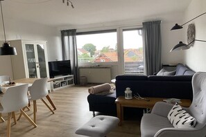 Ein modernes Wohnzimmer mit einer Couch, Hocker und einem Essbereich mit Stühlen.