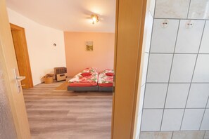 Une pièce avec un lit, un petit radiateur, un panier et une porte.