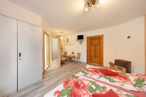 Un dormitorio con una cama, un armario de madera, un televisor en la pared y una puerta que da a otra habitación.