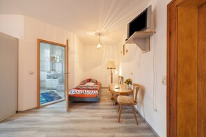 A bedroom with a bed, a desk, a chair, a TV, and a bathroom visible through an open door. - Apartment 'Dreibettzimmer Am See' with Shared Terrace, Shared Garden and Wi-Fi (Schkeuditz)