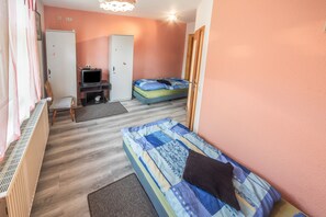 A room with two beds, a desk with a computer, a wardrobe, and a radiator.