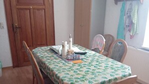 Uma sala de jantar com mesa posta para quatro, cadeiras de madeira, um armário e uma janela com cortinas.