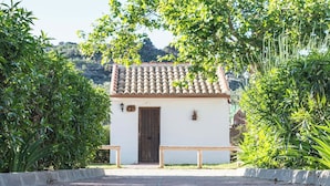 Un petit bâtiment avec un toit en tuiles, une porte en bois et un banc devant.