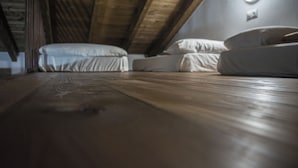 Een kamer met een schuine hemel, houten vloer en een bed met witte lakens.