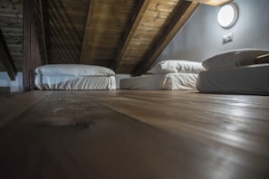 Quarto com teto inclinado, piso de madeira e cama com roupa de cama branca.