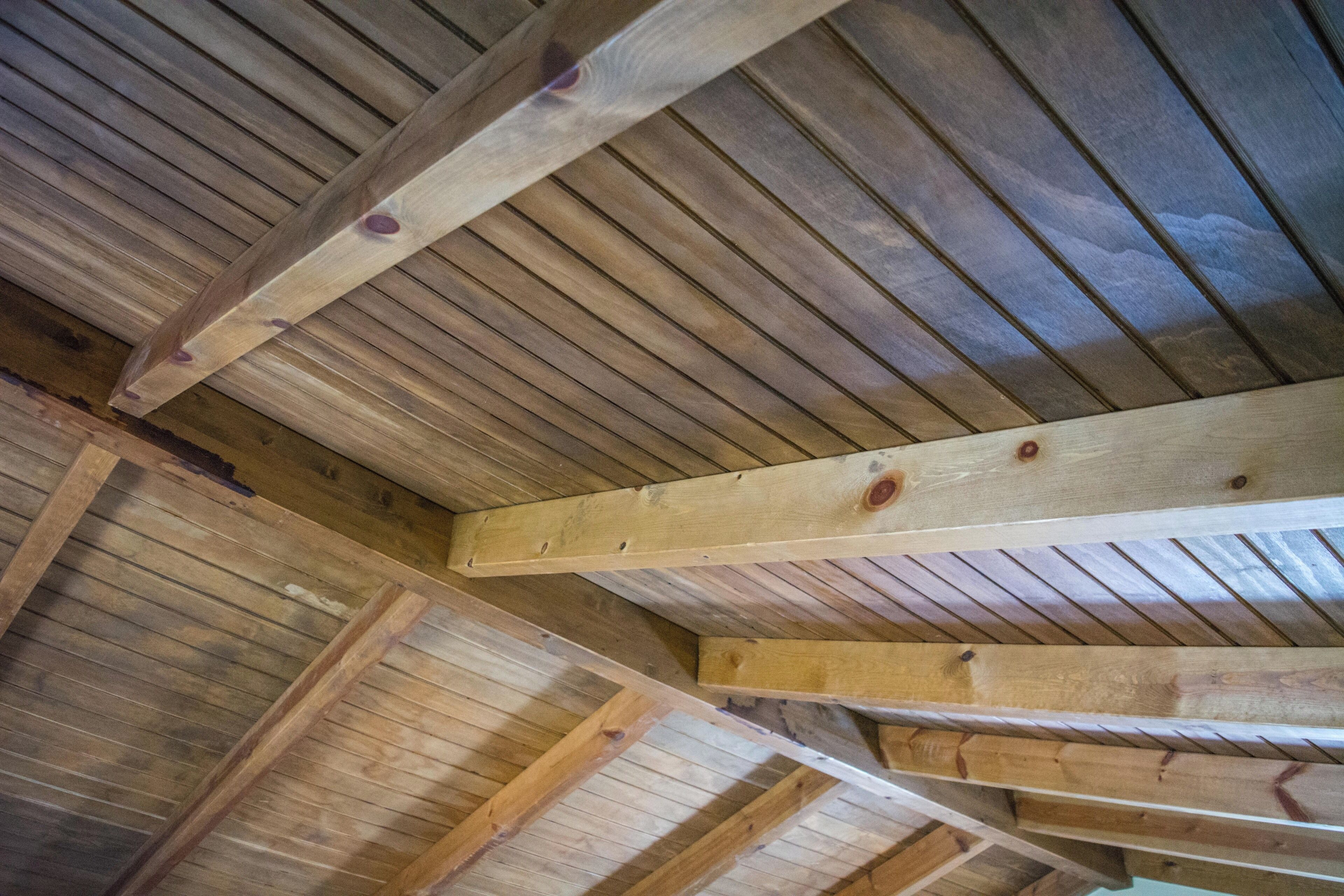 Un plafond en bois avec des poutres apparentes et une structure de toit inclinée.