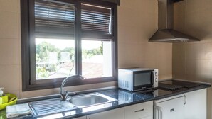 Een keuken met een raam, een magnetron, een spoelbak en kasten.
