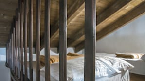 Een kamer met een schuine plafond en houten balken, met een bed met witte beddengoed en een kussen.