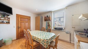 A dining area with a table set for four, wooden chairs, a wooden door, a window with blinds, and a kitchen area with a sink and countertop.