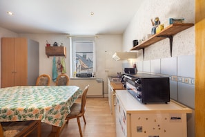 Een kleine keuken met een eettafel, stoelen, een fornuis en een raam met zonwering.