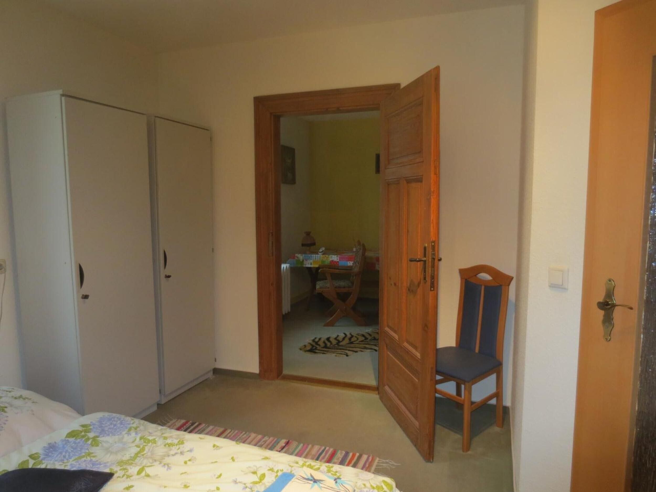 Une chambre à coucher comprenant un lit, une armoire, une chaise et une porte donnant sur une autre pièce.