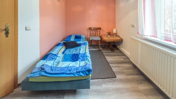 A narrow room with a single bed, a chair, a small table, and a radiator.