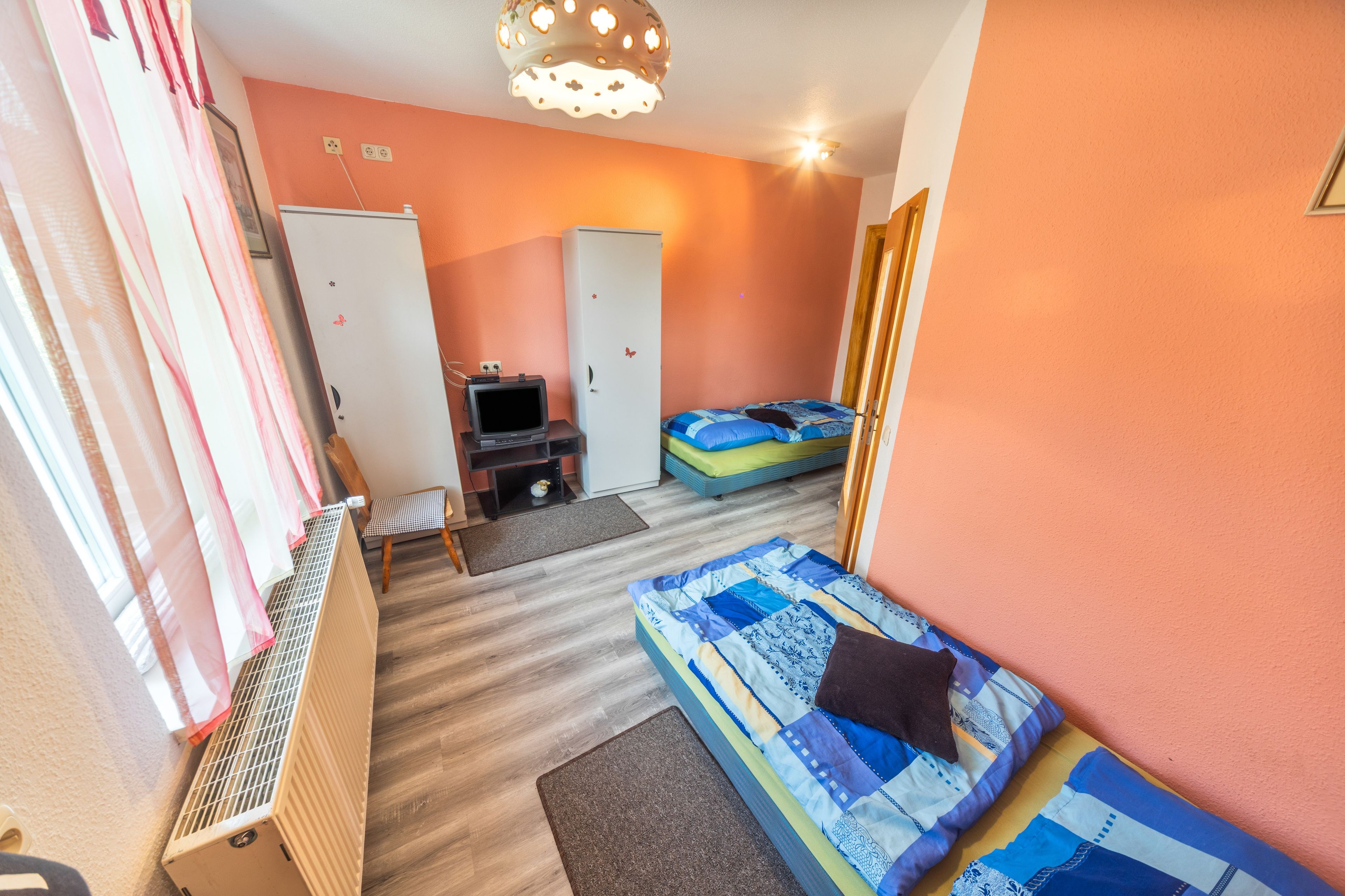 Ein Zimmer mit einem Bett, einem kleinen Schreibtisch mit Computer, einem Heizkörper und einem Kleiderschrank.