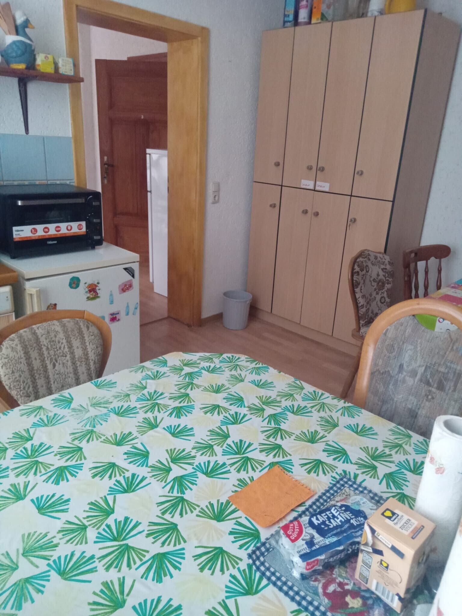Une pièce comprenant une table à manger, des chaises, un réfrigérateur, une armoire et une poubelle.