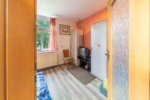 Een kamer met een bed, een televisie op een dressoir, een radiator, een raam met gordijnen en een deur.