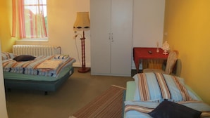 Un dormitorio con dos camas, un armario, una mesa con mantel rojo y una lámpara.