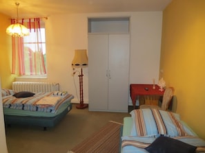 Een slaapkamer met twee bedden, een kledingkast, een tafel met een rode tafelkleed en een lamp.