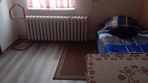 Une pièce avec un radiateur, une fenêtre avec des rideaux, un lit recouvert d’une couvre-lit à rayures bleues et blanches, et un tapis à motifs sur le sol.