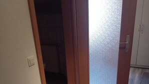 Un couloir avec une porte en bois, un sol carrelé et une zone recouverte de moquette.